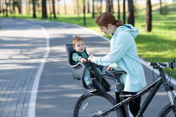 Obraz premium Caucasian woman rides bicycle with one-year-old son in park. 
