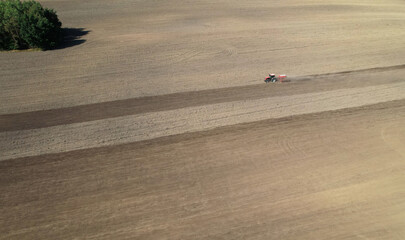 Aerial view of a tractor working on a vast plowed field, preparing the soil for planting. The image captures agricultural machinery in action, symbolizing farming and rural landscapes