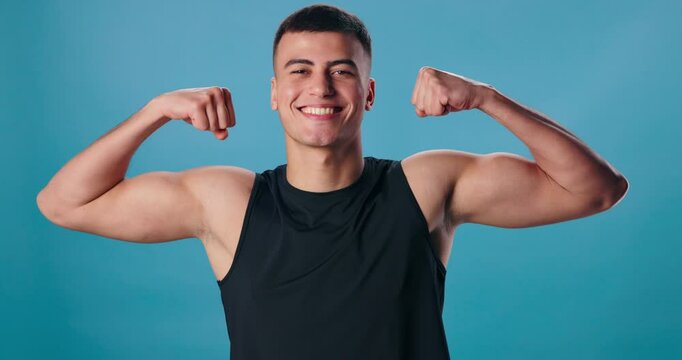 Face, flexing arms and man with power, fitness and progress on blue studio background. Portrait, happy person and model with bicep, strength or wellness with energy, proud or workout with results