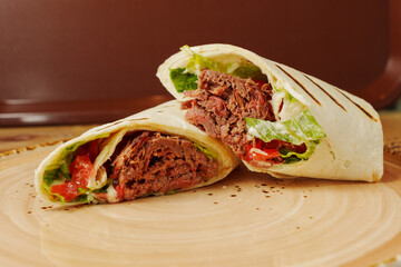 A delicious and hearty wrap filled with succulent beef, fresh veggies, and zesty sauces served on a rustic wooden plate