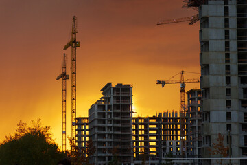 Golden sunset behind a bustling construction site with cranes and buildings silhouetted against the...