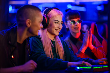 Gamer girl playing mmo rpg in cybercafe while her friends cheering.