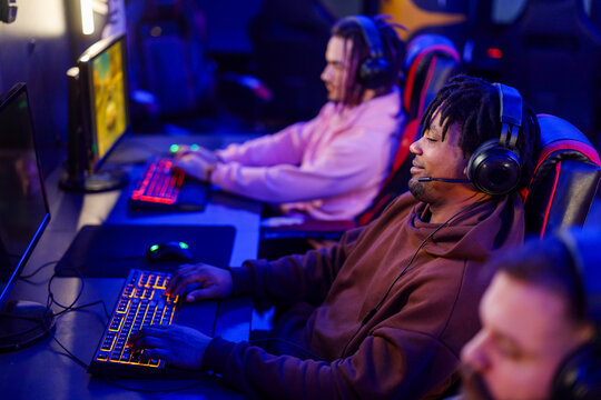 Interracial gamer with headset playing mmo game in internet cafe.