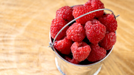 fresh raspberries or strawberries in a bucket on a wooden background