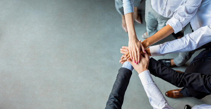 Teambuilding And Togetherness. Unrecognizable Business People Holding Hands Standing In Modern Office. Panorama, Above View, Empty Space