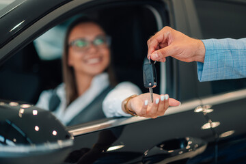 Smiling woman receives car keys, man in blue suit hands over in a car dealership