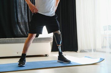 Full length portrait of man with prosthetic leg doing stretching exercises at home and reaching toes