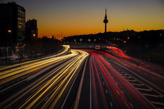 Traces of car lights at dusk driving along the Madrid ring road with the Piruli in the background