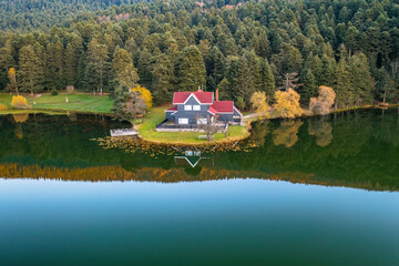 Fototapeta premium Aerial photo of a wooden lake house on the water in the forest taken with a drone. Harmony of blue and green. Golcuk Nature Park Bolu, Turkey.