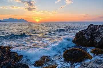 Obraz premium Sunset over the ocean with waves crashing on rocky shore