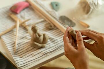 Detail of hands sculpting clay figurine on worktable