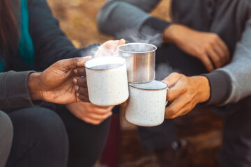 Hands of international hikers cheering up with camping cups, camping in forest, close up