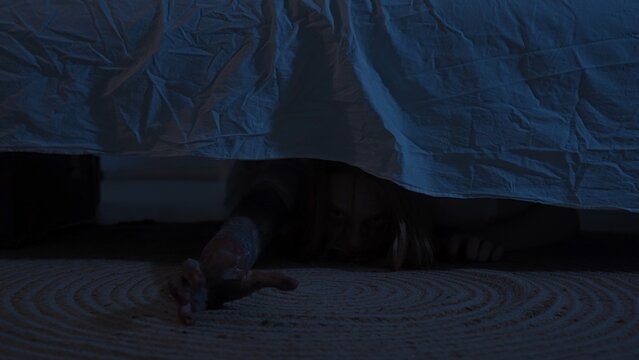 Scary ghost or monster hiding under bed in dark bedroom at night. Scary horror ghost peeking out from under the bed. Halloween Horror Concept.