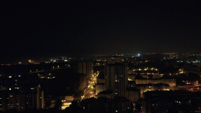 Vista a&eacute;rea noturna da cidade capturada por drone, destacando arranha-c&eacute;us iluminados e as luzes movimentadas das ruas abaixo