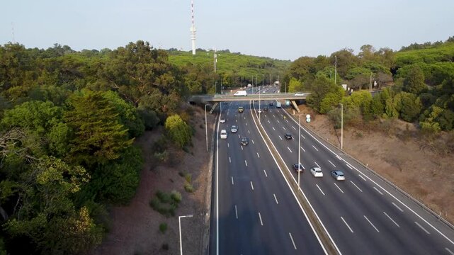 Autoestrada em Monsanto, Lisboa, ao p&ocirc;r do sol com tr&aacute;fego em movimento. O c&eacute;u alaranjado ilumina a estrada e os ve&iacute;culos, criando um contraste entre a natureza e a paisagem urbana.