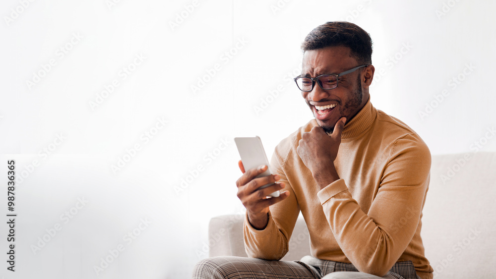 Sticker Happy African American Guy Using Smatphone Chatting In Social Media Or Reading News Sitting On Sofa At Home. Selective Focus