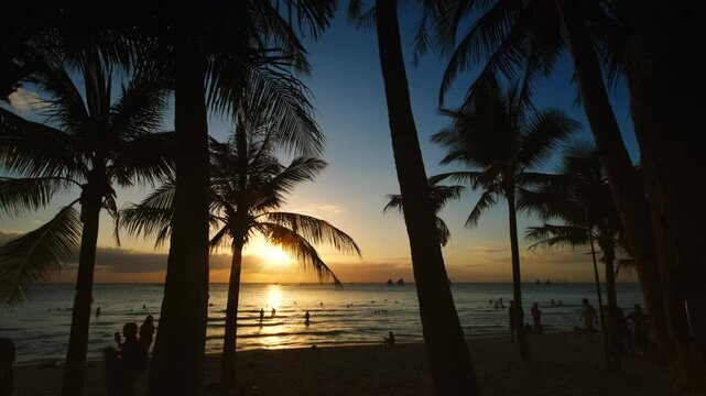 Silhouetted people and palms near sea. Sunset at tropical White beach, Boracay island, Philippines, slow motion 4k
