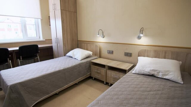 Beds with linen and nightstands in minimalist dormitory room. Children education facility with students bedroom. Comfortable interior