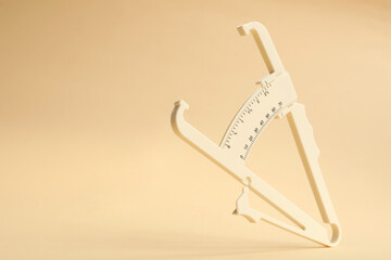 Plastic body fat caliper on beige background. Space for text