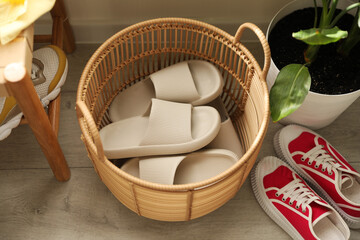 Basket with slippers for guests and sneakers in entryway at home, above view