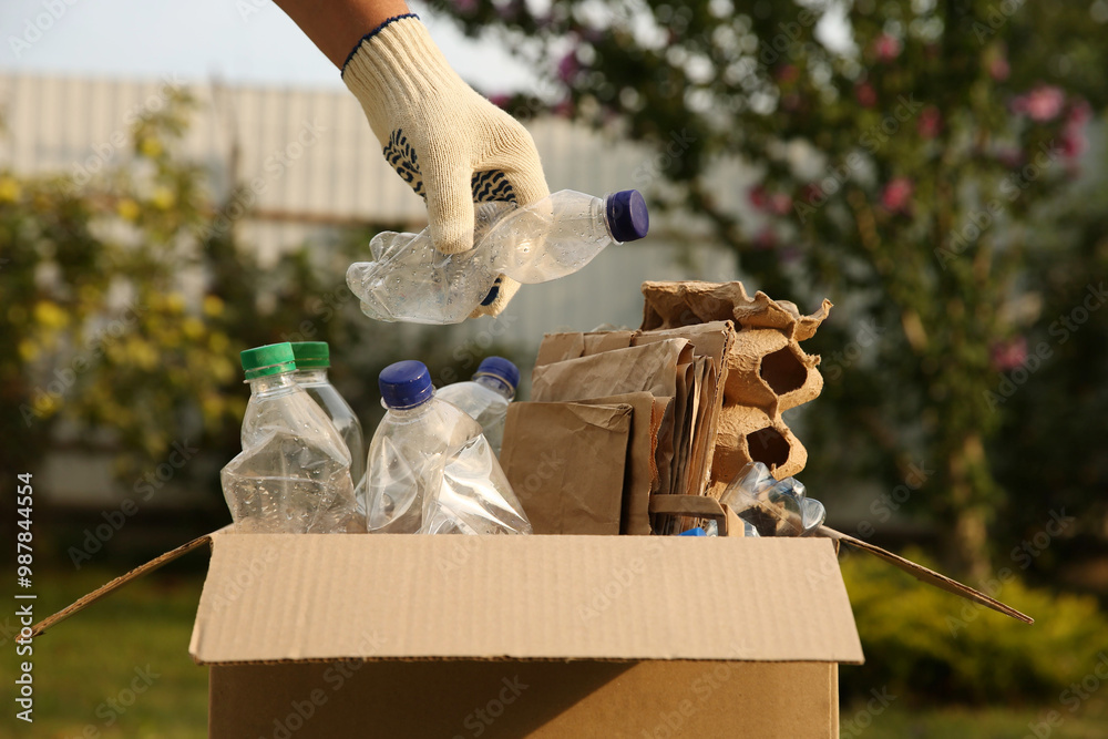 Sticker Recycling concept. Man putting plastic bottle into cardboard box outdoors, closeup