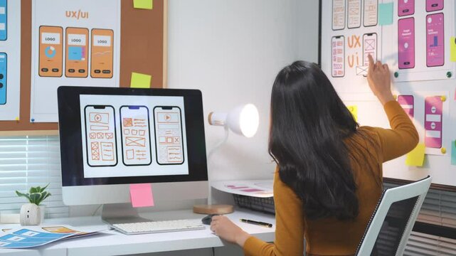 Web designer focuses on enhancing user experience for a mobile application while working in an office environment. Creative processes unfold at the desk, utilizing technology and design skills
