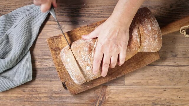Chef cuts a bread with a knife on a wooden kitchen board for healthy dinner, top view. Process of making gazpacho soup