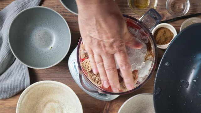 Process of making gazpacho soup. Cook puts ice in blender for making healthy cold tomato soup, top view