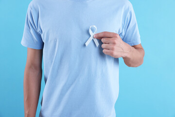 Prostate cancer awareness. Man with light blue ribbon as symbol of support on color background,...