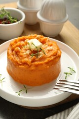 Plate with tasty mashed sweet potato, butter, thyme and walnuts served on table, closeup