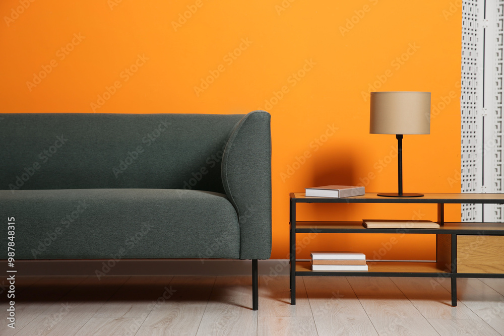 Sticker Stylish sofa and lamp with books on coffee table near orange wall