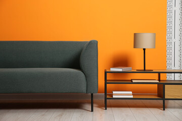 Stylish sofa and lamp with books on coffee table near orange wall