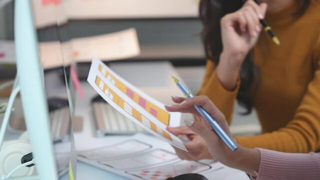 Two ux designers are collaborating on a mobile app interface, pointing at a paper prototype and discussing the user flow and design elements