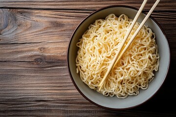Bird s eye view of plain Asian noodles in a bowl with chopsticks on a wood table
