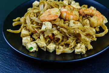 Black plate with pad thai on a slate board
