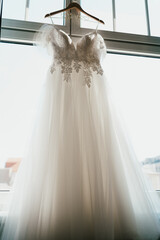 Elegant White Wedding Dress with Floral Embroidery Gracefully Displayed by a Window
