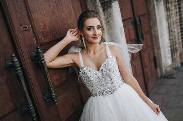 Beautiful smiling bride curly blonde in white lace long dress stands, walks against the background...