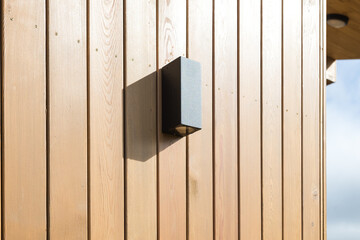 black front lamp on the wooden facade of the house on a sunny day