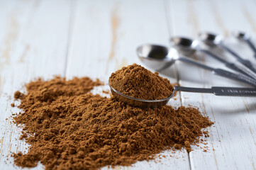 cinnamon powder poured out of a measuring spoon on a white wooden table.