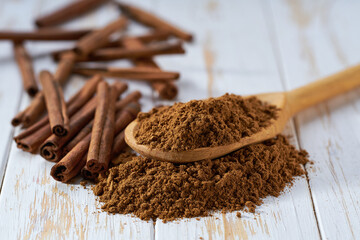 cinnamon powder poured out of a wooden spoon on a white wooden table, selective focus.