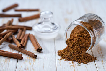 cinnamon powder poured out of a glass jar on a white wooden table, selective focus.