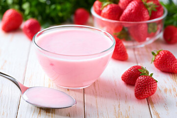strawberry smoothie in a clear glass bowl with spoon on a white table, selective focus.