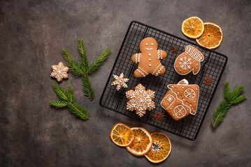 Set of Christmas gingerbread cookies on a cooling rack with dried orange slices and spruce branches, brown rustic background. Top view, flat lay, copy space.