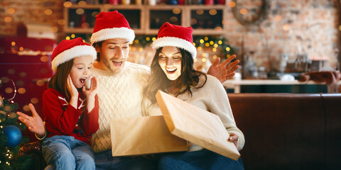 Christmas miracle. Surprised family of three looking into shining gift box, opening xmas presents together, kitchen interior