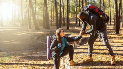 Attractive african hiker helping his girlfriend uphill in the countryside