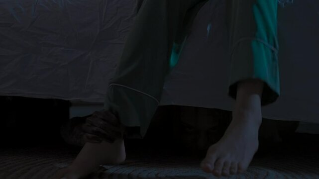 Woman sleeping in bed in dark apartment room, monster hiding under bed and catches girl's legs when female stands up. Halloween horror concept.