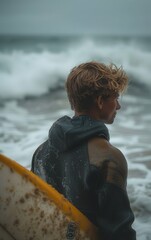 Fototapeta premium A man is standing on the beach with a surfboard in his hand. He is wearing a black jacket and he is wet. Scene is relaxed and casual, as the man is enjoying his time at the beach