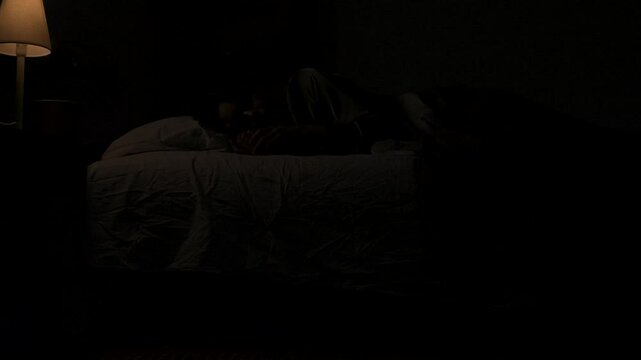 Woman sleeping in bed in dark apartment room, monster hiding under bed. Storm and lightning flash lights outside. Halloween horror concept.