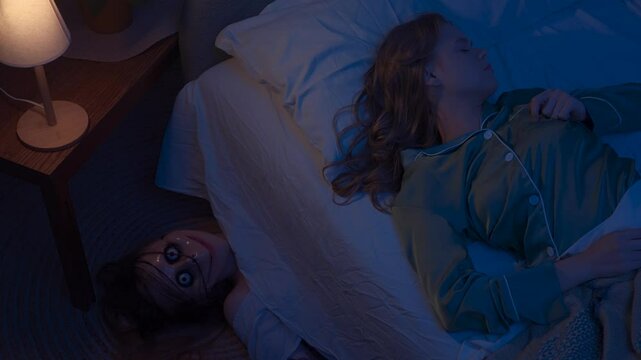 Woman sleeping in bed in dark room, monster hiding under bed. scary ghost woman laying on the floor with creepy face and scares girl. Halloween horror concept
