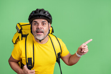Delivery man in yellow shirt pointing with surprised expression on green chroma background.